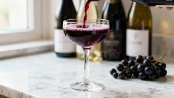 Un verre de vin rouge est servi, avec des grappes de raisin noir à côté. Le vin aligoté, souvent blanc, ici rouge, évoque la fraîcheur et la vivacité.