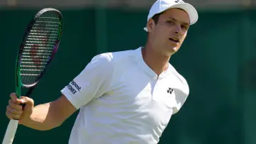 Hubert Hurkacz w białej koszulce i czapce, gotowy do uderzenia rakietą na Wimbledonie.