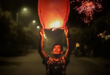 Chłopiec wypuszcza lampion życzeń w noc sylwestrową, podczas gdy fajerwerki rozświetlają niebo. Nowy rok w pełni!