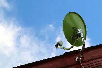 Zielony talerz do satelity zamontowany na drewnianej ścianie, skierowany ku błękitnemu niebu z chmurami.