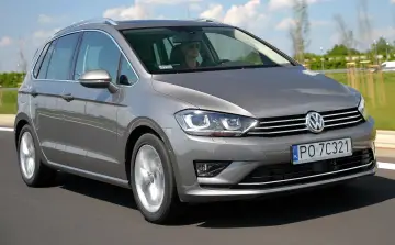 Szary Volkswagen Sportsvan jedzie po drodze, kierowca w okularach prowadzi auto.