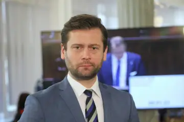 Minister sportu w niebieskiej marynarce i krawacie w paski, z zarostem, patrzy prosto w obiektyw.
