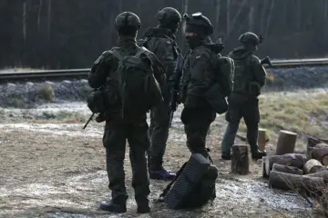 Żołnierze w kamuflażu stoją przy torach kolejowych. Zastanawiasz się, ile zarabia szeregowy w wojsku?