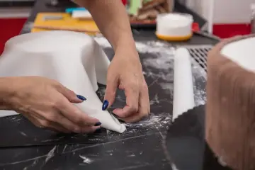 Hände formen weißen Fondant für eine Torte. Hier sind Tipps zum Fondant ausrollen für perfekte Ergebnisse.
