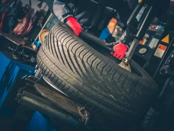 Mechanik w czerwonych rękawiczkach manipuluje oponą. Zastanawiasz się, ile waży opona do samochodu osobowego?