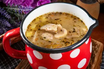 Pyszna zupa grzybowa z kawałkami mięsa i ziemniaków w czerwonym kubku w białe kropki. Zastanawiasz się, ile można trzymać zupę w lodówce?
