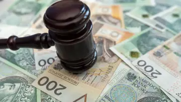 Młotek sędziowski na stosie polskich banknotów. Określenie "stawka dzienna kk" może sugerować koszty sądowe lub kary finansowe.