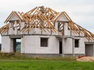 Budowa domu 120m2 w stanie surowym otwartym. Widoczne ściany z bloczków, konstrukcja dachu z drewna.