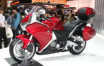 Błyszczący, czerwony motocykl Honda VFR 1200 z kuframi, prezentowany na wystawie motoryzacyjnej.