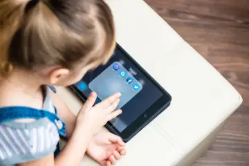 Dziecko dotyka ekranu tabletu z ikonami aplikacji społecznościowych, w tym Facebooka. Zastanawiam się, od ilu lat jest Facebook i czy to już dla niego?