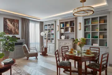 Elegancki salon w stylu klasycznym. Okrągły stół z krzesłami, regały z książkami, fotel i obraz tworzą przytulną atmosferę.