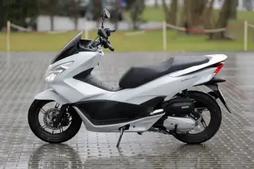 Biały skuter Honda PCX na mokrym bruku. Idealny na pierwsze samodzielne przejażdżki, bo od ilu lat można jeździć 50?