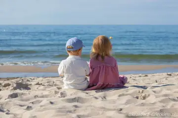 Dwoje dzieci siedzi na plaży, patrząc na morze. Idealne miejsce, gdzie z dzieckiem na weekend.