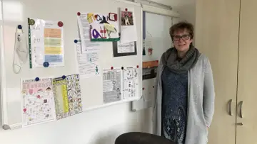 Lehrerin mit Lernmaterialien, darunter ein Kreuzworträtsel mit Gegenteilen und eine Liste von Verben, die das present participle zeigen.