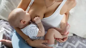 Ciepły moment karmienia piersią. 3 miesięczne dziecko z zaciekawieniem spogląda na świat, ssąc mleko mamy.