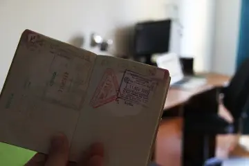 Otwarty paszport z pieczątkami z Meksyku i Malezji. W tle biurko z laptopem. Ile cyfr ma paszport?
