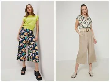 Dwie kobiety prezentują modne spódnico spodnie długie. Jedna w kolorowe spodnie w owoce, druga w beżowe, eleganckie.