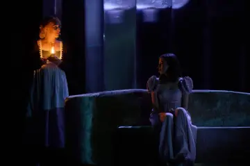 Dwie kobiety na scenie, jedna z lampą, druga na kanapie. Scena jak z teatrum mundi, pełna mroku i tajemnicy.