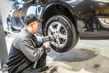 Mechanik używa klucza udarowego, by zdjąć zapieczone koło z podniesionego samochodu.
