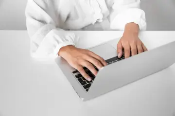 Osoba w białej bluzce pisze na laptopie, przygotowując zaświadczenie o niezaleganiu.