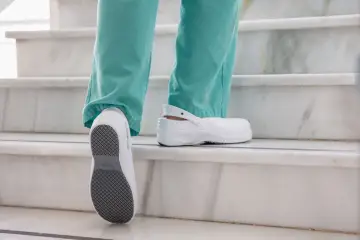 Persona subiendo escaleras con zapatos blancos, mostrando la suela antideslizante. El poliuretano en zapatos ofrece comodidad y durabilidad.