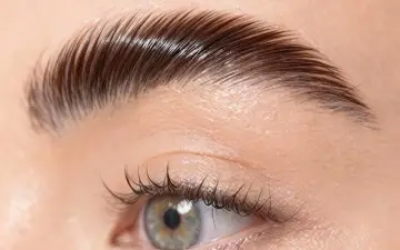 Un gros plan sur un œil et un sourcil parfaitement plaqué, montrant comment plaquer ses sourcils pour un look impeccable.