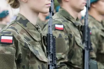 Żołnierze w mundurach z polskimi flagami, gotowi do marszu. Słychać przyśpiewki wojskowe.