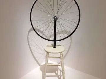 Roue de vélo fixée sur un tabouret, une œuvre emblématique de Marcel Duchamp, projetant une ombre fascinante.