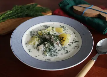 Zupa śledziowa z ziemniakami i koperkiem w talerzu, obok łyżka i pęczek koperku.