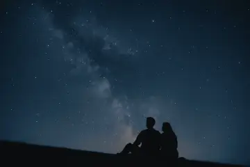 Un couple en silhouette admire la Voie lactée. Une idée de rendez-vous romantique parfait sous les étoiles.