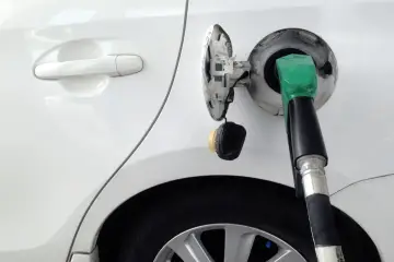 Tankowanie białego samochodu z użyciem bezkorkowego systemu wlewu paliwa. Zielona dysza dystrybutora w otworze wlewu.
