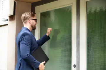 Mężczyzna w garniturze puka do drzwi, niosąc teczkę. Zastanawia się, ile zabierze komornik z premii.