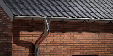 Błyszczący łącznik do rynny odprowadza wodę z dachu na ceglanym budynku.