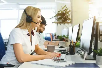 Kobieta w słuchawkach z mikrofonem pracuje przy komputerze w biurze.