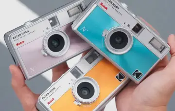 Trzy kolorowe aparaty Kodak Ektar H35N leżą w dłoni. Dowiedz się, jak wywołać zdjęcia z aparatu jednorazowego.