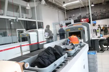 Kontrola paszportowa na lotnisku. Bagaże przechodzą przez skaner, a podróżni czekają na swoją kolej.