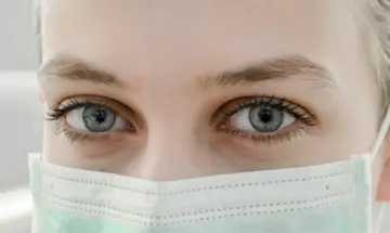 Szare oczy, lekko nieostre widzenie po laserowej korekcji wzroku, pod zieloną maseczką ochronną.
