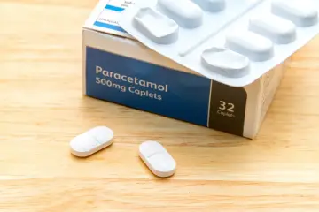 Opakowanie paracetamolu 500mg i dwie tabletki na drewnianym tle. Szybka ulga w bólu zęba.
