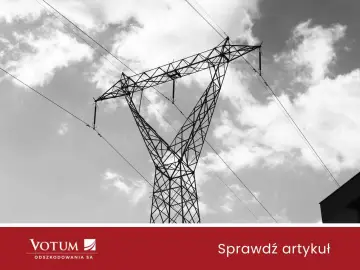 Wysoki słup energetyczny na działce, z którego zwisają kable, na tle chmur.