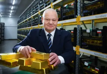 Mężczyzna w garniturze w magazynie Narodowego Banku Polskiego, trzymający sztabki złota. Pokazuje, ile złota ma Polska.