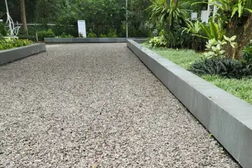 Un chemin de gravier cours maison, bordé de pierres grises et de verdure luxuriante, invite à la promenade.
