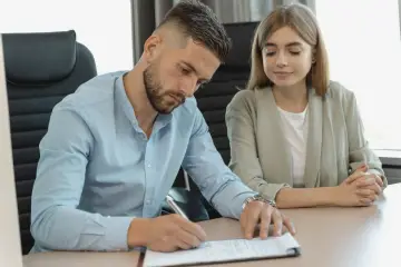 Mężczyzna podpisuje dokumenty dotyczące ustanowienia odrębnej własności lokalu, kobieta patrzy z uwagą.