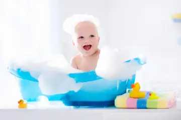 Uśmiechnięte dziecko w pianie w niebieskiej wanience. Ciekawi Cię, jak szybko rosną włosy u dzieci?