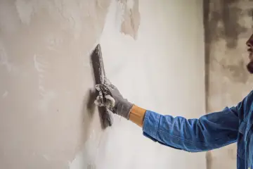 Ręka w rękawicy nakłada tynk na ścianę. To kluczowy etap, by wiedzieć, jak obliczyć powierzchnię tynków wewnętrznych.