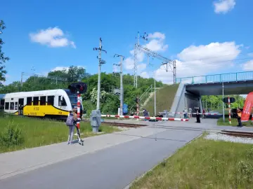 Dziewczynka na hulajnodze czeka przy przejeździe kolejowym PKP, gdy nadjeżdża pociąg.