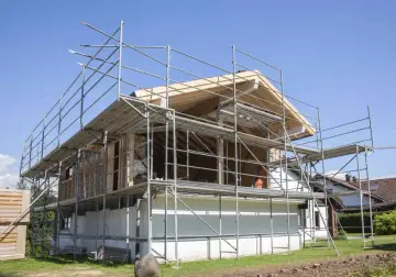 Budowa dobudówki do starego domu. Widać rusztowania, drewnianą konstrukcję dachu i białe ściany.
