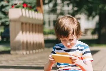 Chłopiec z telefonem w ręku, który może pomóc w ustaleniu, jak śledzić lokalizację dziecka.