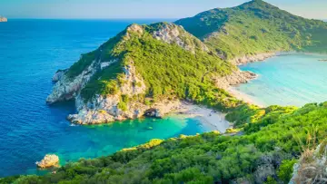 Idealna Grecja na wakacje: malownicza zatoka z piaszczystą plażą, turkusowa woda i zielone wzgórza.