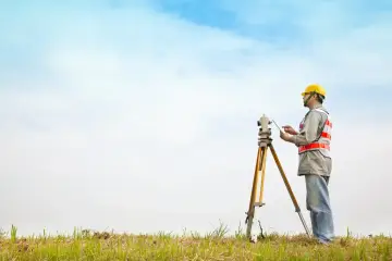 Geodeta w kasku i kamizelce odblaskowej używa tabletu do precyzyjnego pomiaru działki.