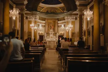 Wnętrze kościoła z wiernymi na ławkach. W tle ołtarz i obraz. Czy to miejsce, gdzie płaci się podatek na kościół?